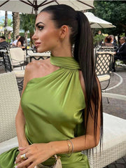 Woman wearing green halter backless off shoulder sleeveless dress with diagonal collar sitting outdoors
