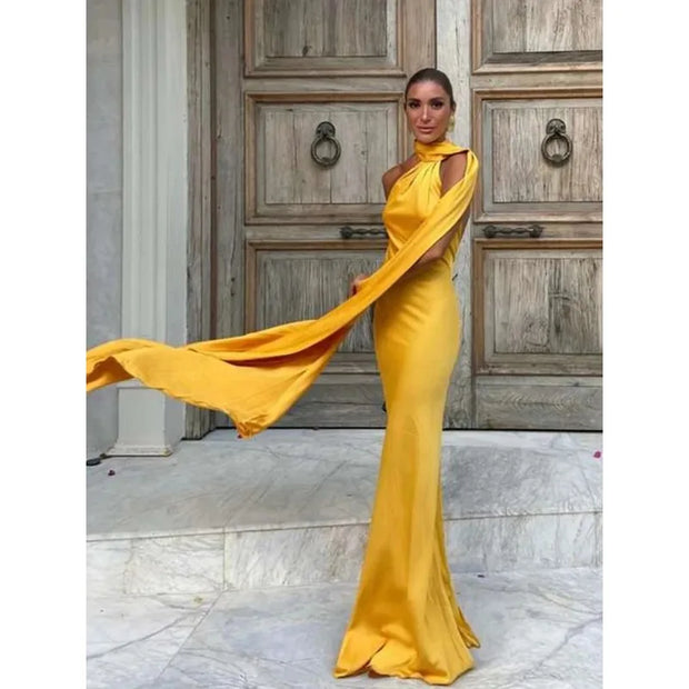 woman wearing yellow sexy backless off-shoulder sleeveless gown with flowing sash standing by wooden doors