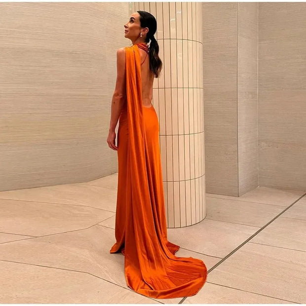 Woman wearing a sleek orange women's sexy backless off shoulder sleeveless gown with a long flowing train standing indoors