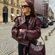 Woman wearing a burgundy faux leather jacket with belt and lapel collar on city street
