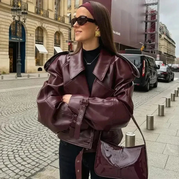 Woman wearing a burgundy faux leather jacket with belt and lapel collar on city street