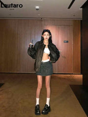 Woman wearing a black soft faux leather zipper jacket with turn-down collar and drop-shoulder sleeves paired with a denim mini skirt and black platform shoes