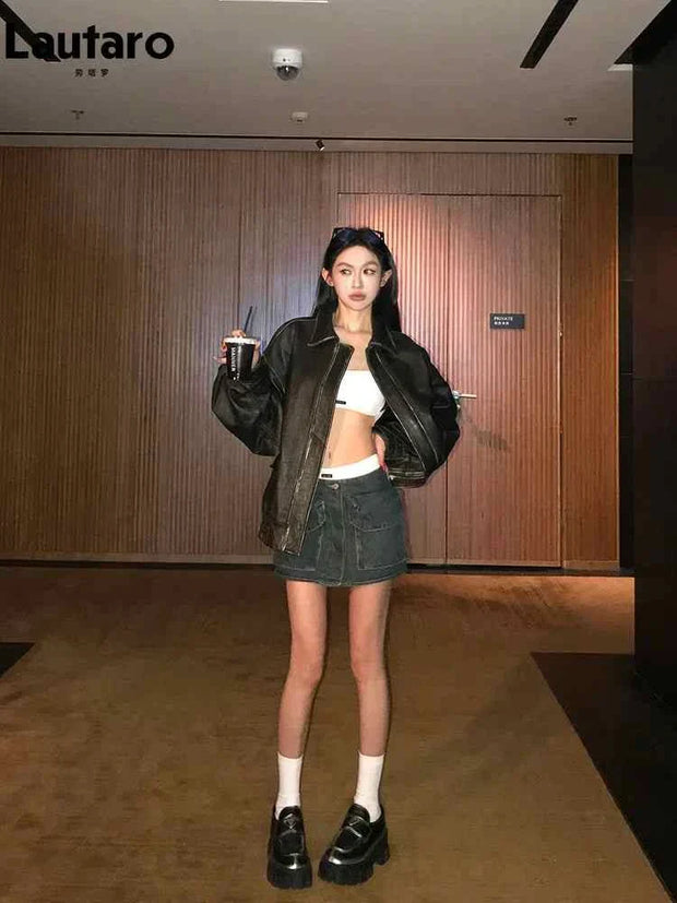Woman wearing a black soft faux leather zipper jacket with turn-down collar and drop-shoulder sleeves paired with a denim mini skirt and black platform shoes
