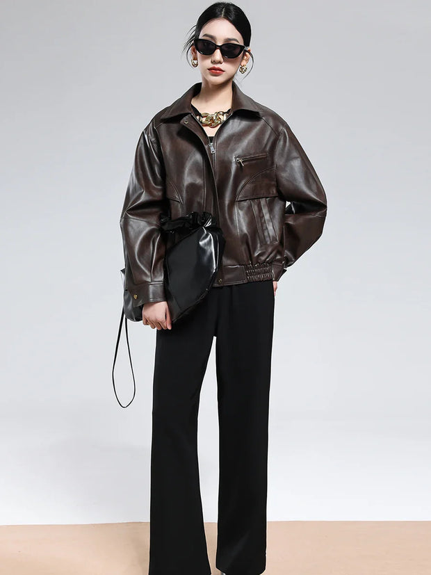 Woman wearing brown PU leather jacket with turn-down collar and zipper, styled with black pants and sunglasses