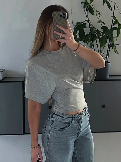 Woman wearing casual gray O-neck corset top and high-waisted blue jeans taking mirror selfie